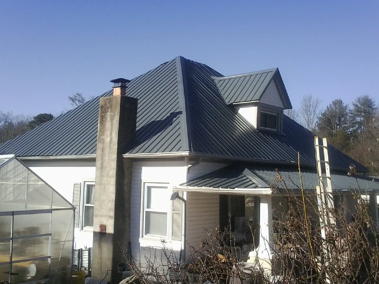 Dark blue standing seam metal roof on a white farmhouse with dormer — Slate & Tile Roof Repair by Roofing Brothers in Spartanburg