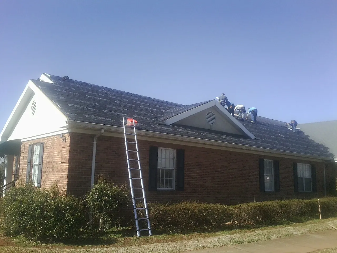 Crew tearing shingles off a brick ranch roof with a ladder set — Emergency Roof Repair work by our crew in Spartanburg