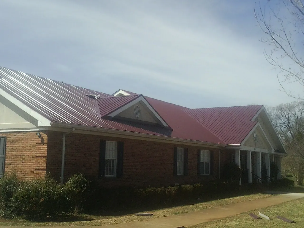 Red metal roof with gabled entries on a long brick building, from a Hail Damage Roof Repair job in Spartanburg