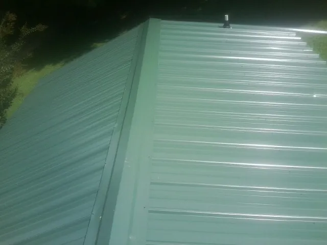 New green metal panels meeting at the ridge of a roof — Flat Roof Repair work by our crew in Spartanburg