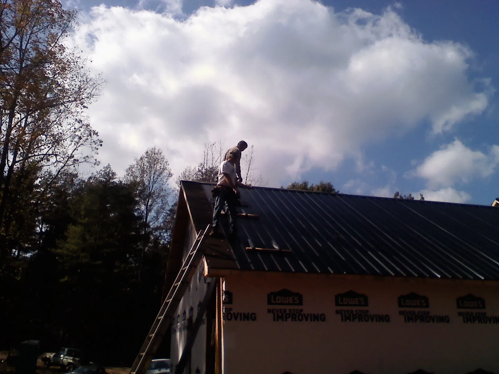 Roofer fastening dark metal panels high against a cloudy sky, from a Roof Inspection job in Spartanburg