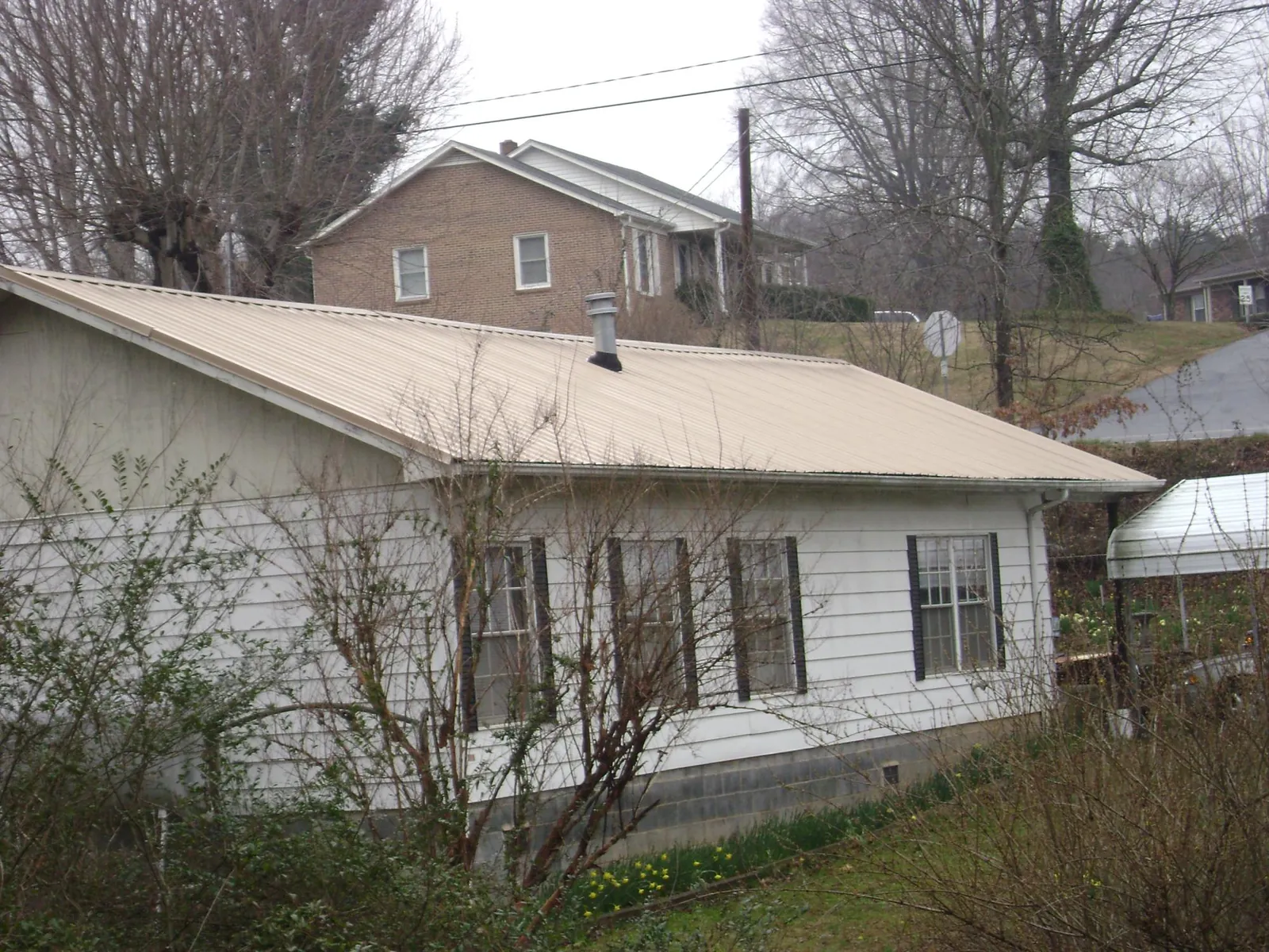 Tan metal roof on a white sided house set into a hillside — Commercial Roofing by Roofing Brothers in Spartanburg